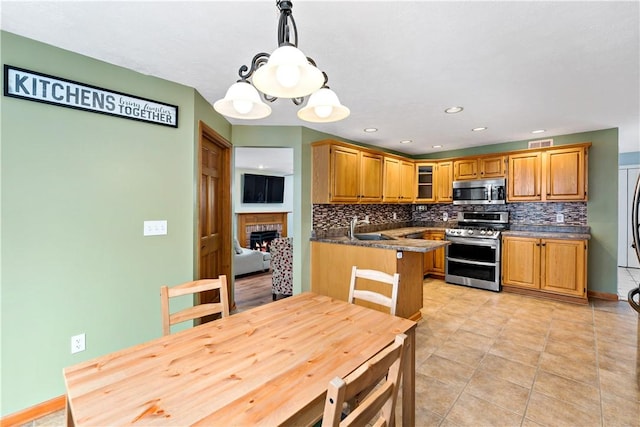 kitchen with sink, stainless steel appliances, kitchen peninsula, decorative light fixtures, and decorative backsplash