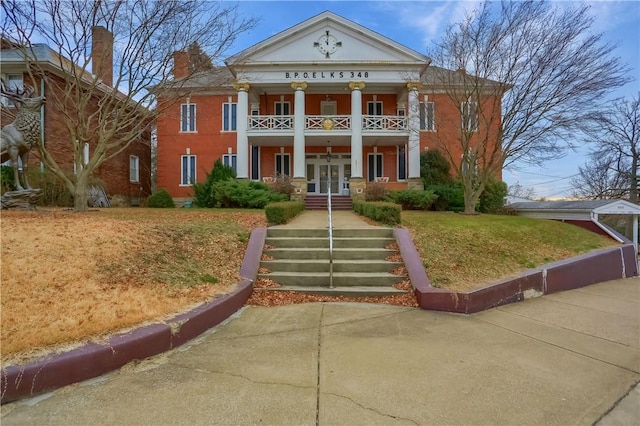 greek revival house with a front lawn, covered porch, french doors, and a balcony