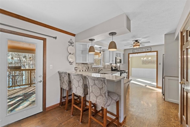 kitchen featuring kitchen peninsula, appliances with stainless steel finishes, a breakfast bar, wood-type flooring, and white cabinets