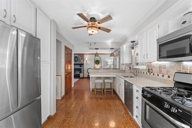 kitchen featuring white cabinetry, sink, wood-type flooring, pendant lighting, and appliances with stainless steel finishes