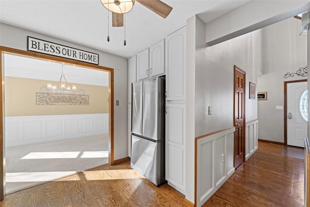 kitchen with pendant lighting, ceiling fan with notable chandelier, white cabinetry, wood-type flooring, and stainless steel refrigerator