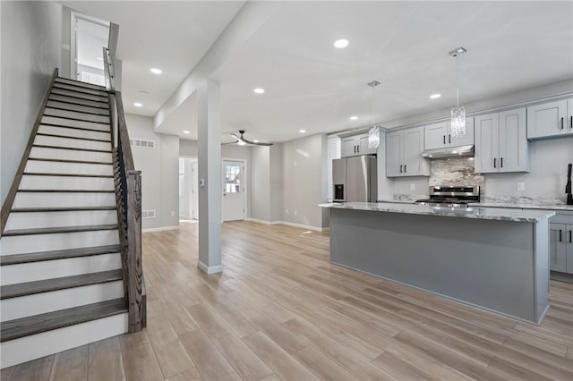 kitchen featuring light stone countertops, gray cabinetry, stainless steel appliances, decorative light fixtures, and a center island