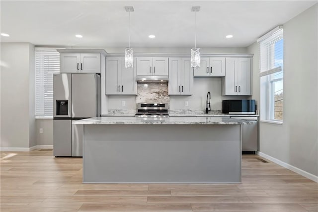 kitchen featuring decorative light fixtures, a kitchen island, light stone counters, and stainless steel appliances