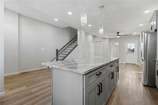 kitchen featuring stainless steel fridge, ceiling fan with notable chandelier, a center island, gray cabinets, and hanging light fixtures