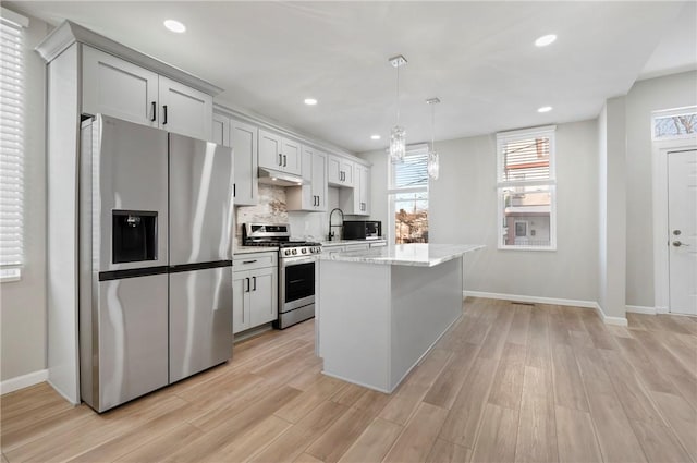 kitchen with light stone countertops, stainless steel appliances, pendant lighting, light hardwood / wood-style flooring, and a kitchen island