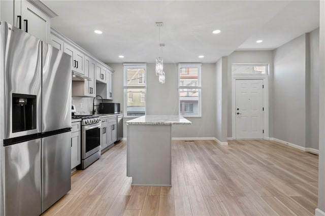 kitchen with light stone countertops, hanging light fixtures, light hardwood / wood-style floors, a kitchen island, and appliances with stainless steel finishes