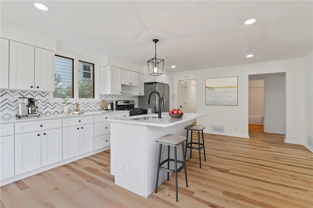 kitchen featuring a kitchen island with sink, white cabinets, hanging light fixtures, and light wood-type flooring