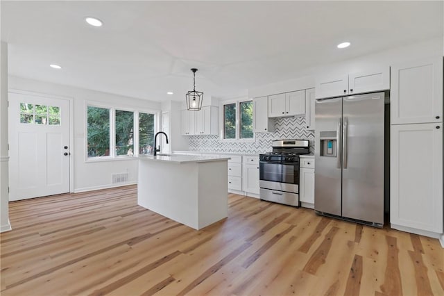 kitchen featuring pendant lighting, light hardwood / wood-style flooring, an island with sink, white cabinetry, and stainless steel appliances