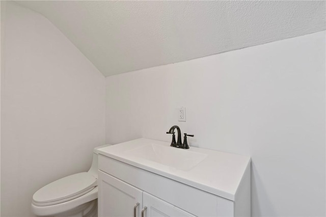 bathroom with toilet, a textured ceiling, vanity, and vaulted ceiling