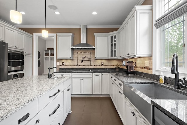 kitchen featuring dark stone countertops, wall chimney range hood, backsplash, and hanging light fixtures