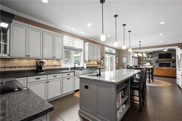 kitchen with dark stone counters, sink, black electric cooktop, an island with sink, and white cabinetry