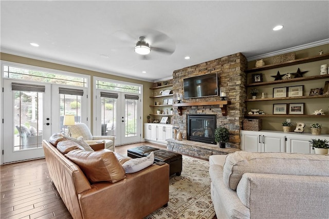 living room featuring french doors, light hardwood / wood-style flooring, ceiling fan, ornamental molding, and a fireplace