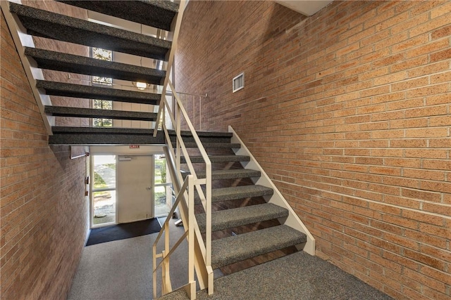 stairs featuring carpet flooring, a towering ceiling, and brick wall