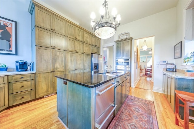 kitchen with stainless steel oven, a kitchen island with sink, decorative light fixtures, a notable chandelier, and light hardwood / wood-style floors