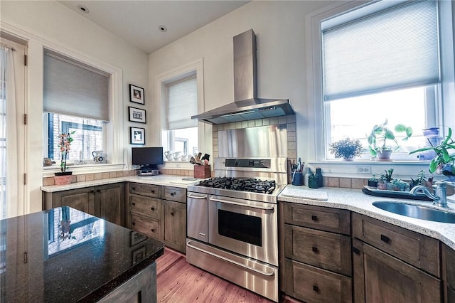 kitchen featuring stainless steel gas range oven, light stone counters, sink, and wall chimney range hood