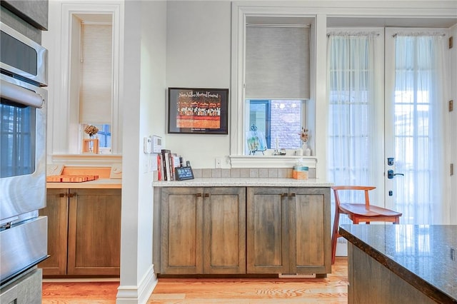 bar with a healthy amount of sunlight, dark stone counters, and light hardwood / wood-style flooring