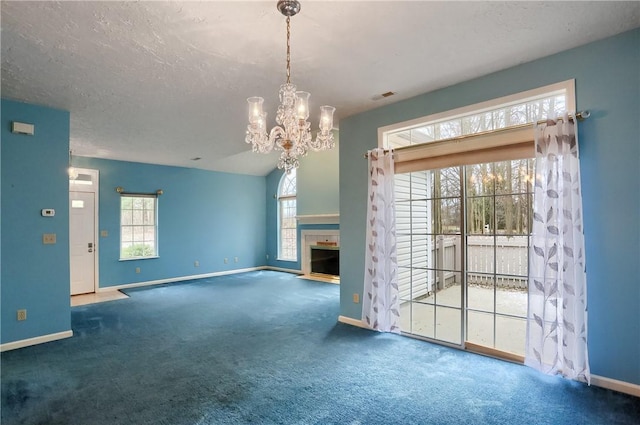 unfurnished living room with carpet flooring, a textured ceiling, a chandelier, and a healthy amount of sunlight