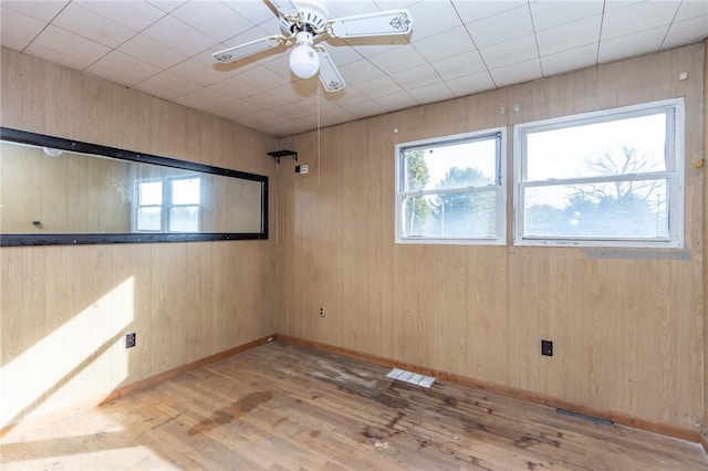 spare room with light wood-type flooring, ceiling fan, and wooden walls