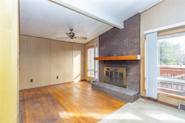 unfurnished living room with wood walls, lofted ceiling with beams, ceiling fan, and a fireplace