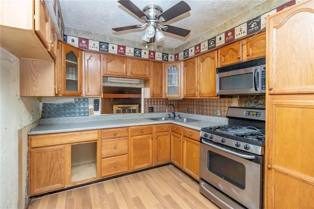 kitchen featuring ceiling fan, sink, a textured ceiling, appliances with stainless steel finishes, and light wood-type flooring