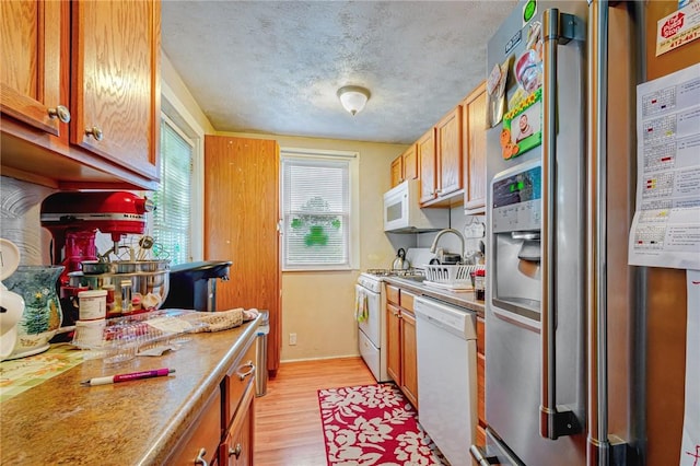 kitchen with light wood-type flooring, a textured ceiling, and white appliances