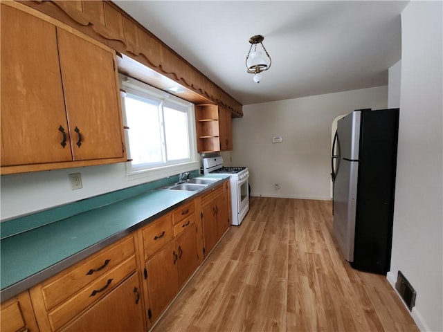 kitchen with sink, white gas range oven, stainless steel fridge, light wood-type flooring, and decorative light fixtures