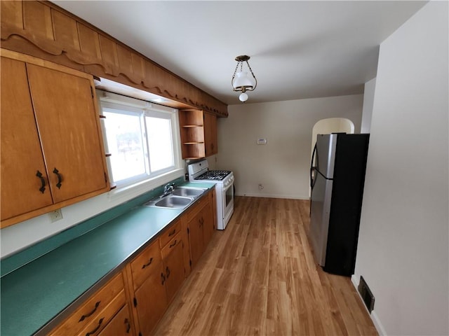 kitchen with stainless steel refrigerator, white gas stove, sink, hanging light fixtures, and light hardwood / wood-style floors