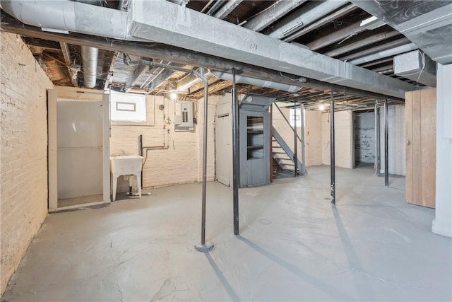 basement with electric panel, sink, and brick wall