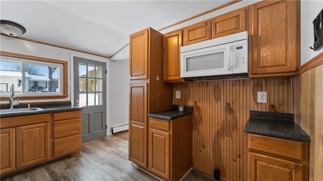 kitchen featuring sink, a baseboard heating unit, crown molding, lofted ceiling, and hardwood / wood-style flooring