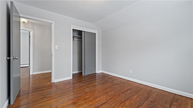 unfurnished bedroom featuring dark hardwood / wood-style flooring, a closet, a baseboard radiator, and vaulted ceiling