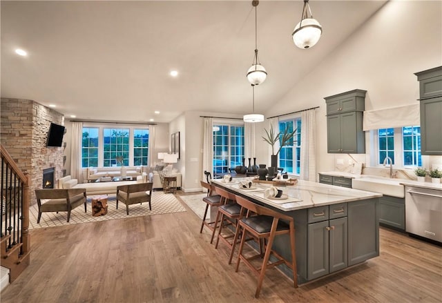 kitchen featuring stainless steel dishwasher, light stone counters, decorative light fixtures, a fireplace, and light hardwood / wood-style floors