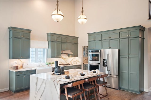 kitchen with green cabinets, sink, light stone countertops, decorative light fixtures, and stainless steel appliances