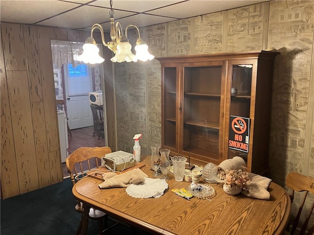 carpeted dining area with a paneled ceiling and a notable chandelier