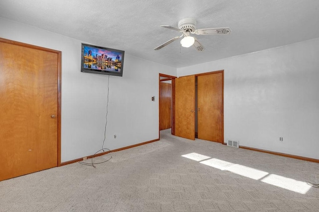 unfurnished bedroom with ceiling fan, light carpet, and a textured ceiling