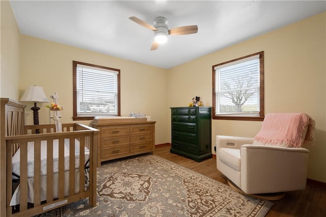 bedroom with wood-type flooring, a nursery area, and ceiling fan