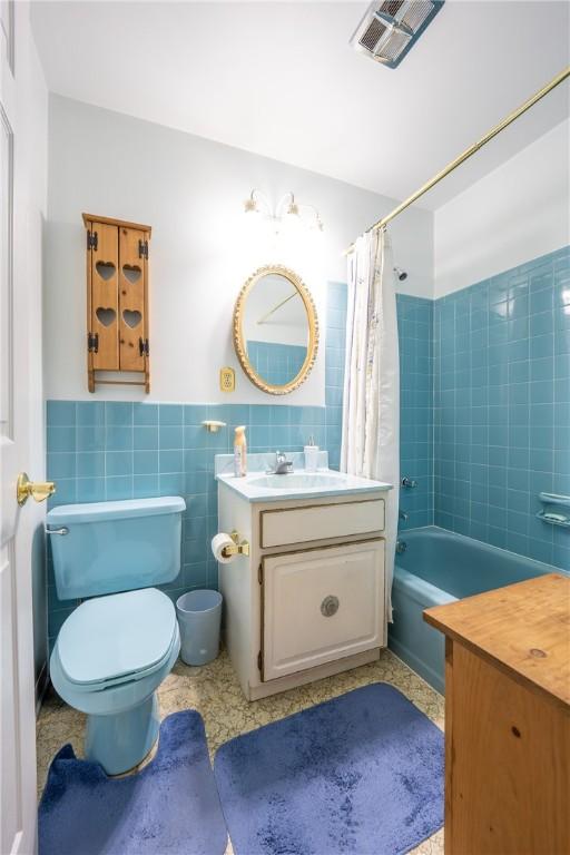 full bathroom with shower / bath combination with curtain, toilet, tile walls, and vanity