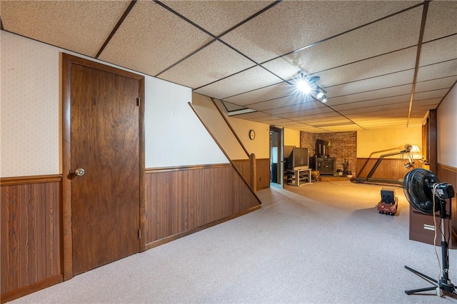 interior space with carpet flooring, a wood stove, wood walls, and a drop ceiling