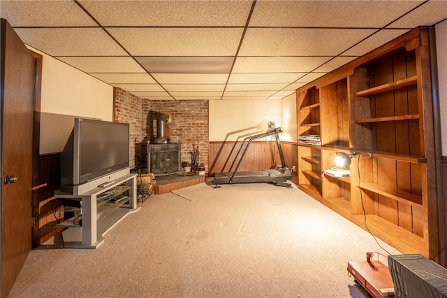 workout area with carpet flooring, a wood stove, built in features, wood walls, and a paneled ceiling