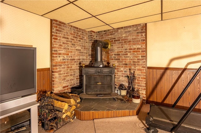 interior space with carpet flooring, a paneled ceiling, a wood stove, and wood walls