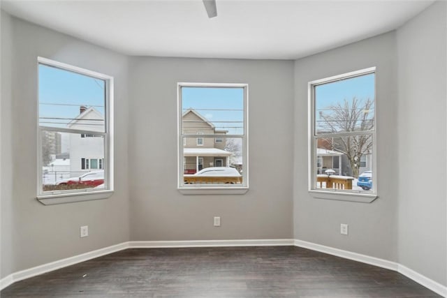 empty room with a healthy amount of sunlight, baseboards, and dark wood-style flooring
