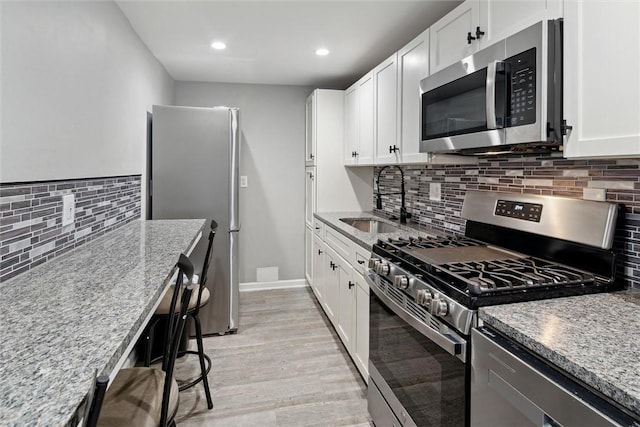 kitchen with stainless steel appliances, white cabinetry, and light stone counters