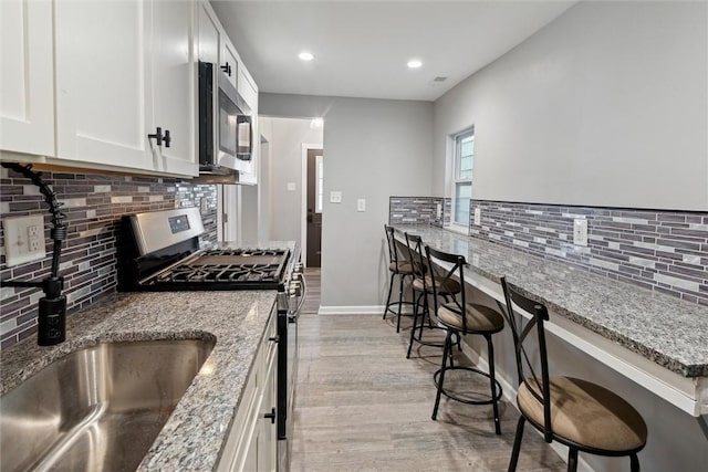 kitchen with light stone countertops, stainless steel appliances, light hardwood / wood-style flooring, white cabinets, and a breakfast bar area