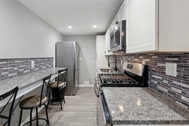 kitchen featuring stone counters, appliances with stainless steel finishes, white cabinetry, and a breakfast bar area