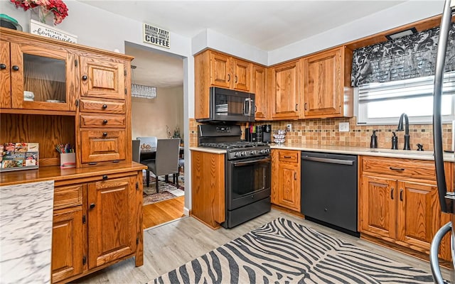 kitchen with backsplash, sink, black appliances, and light hardwood / wood-style floors