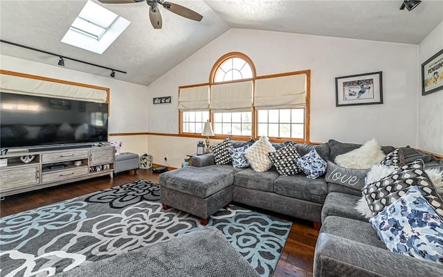 living room with dark hardwood / wood-style floors, track lighting, ceiling fan, and vaulted ceiling with skylight