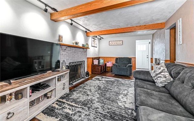 living room featuring beam ceiling, track lighting, a brick fireplace, and wooden walls