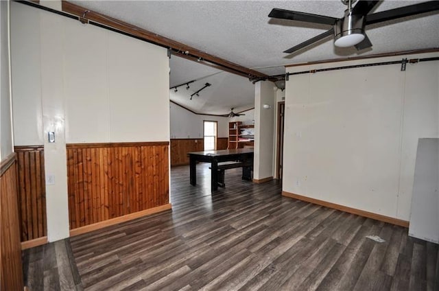 interior space with lofted ceiling, dark wood-type flooring, track lighting, ceiling fan, and a textured ceiling