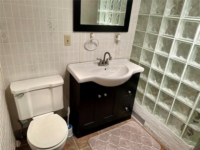 bathroom with toilet, vanity, tile patterned floors, and tile walls