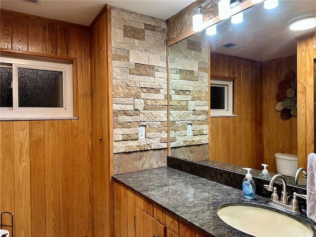 bathroom with vanity, wood walls, and toilet