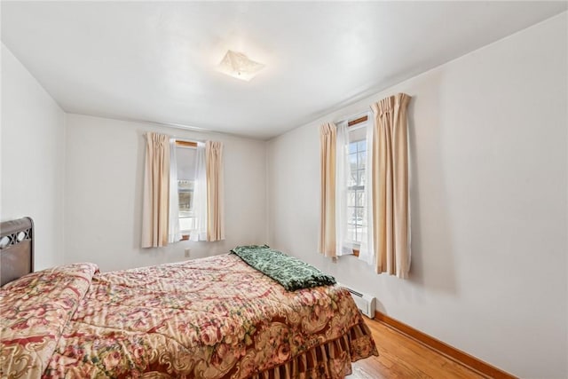 bedroom featuring hardwood / wood-style floors and a baseboard heating unit